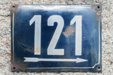 Weathered grunge square metal enameled plate of number of street address with number 121 closeup