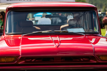 old classic antique American red car front, view of the windscreen, hood, roof, and interior, with people in the background during outdoor cars show