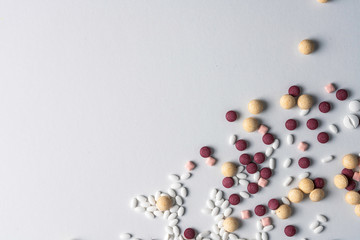 Multi colored pills scattered around on white table. To simulate drug abuse, medical concept, healthcare and prescription. Hospital, sickness and medicine theme.