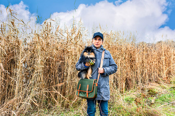 Girl with charming Pomeranian spitz dog in high grass in summer autumn forest park.