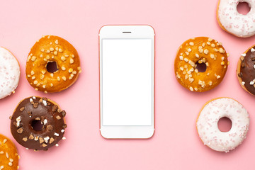 Mobile phone and sweet chocolate, caramel and strawberry donuts on pink background flat lay