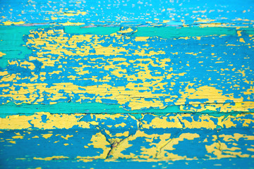 Yellow-blue-green peeling paint texture. A wooden surface covered with several layers of cracked paint