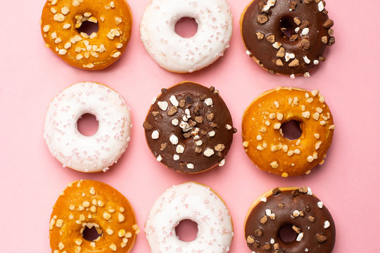 Sweet chocolate, caramel and strawberry donuts on pink background flat lay