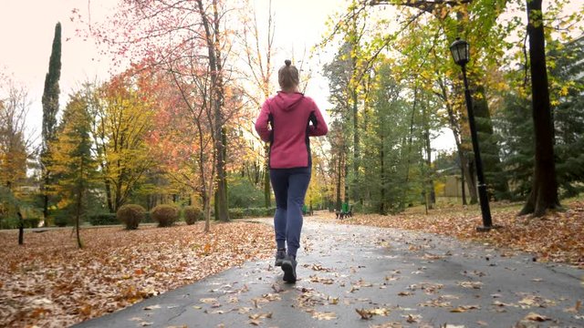 athletic young girl running in autumn Park after rain. rear view