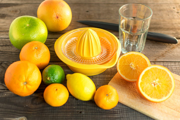 halbierte Orange mit verschiedenen Zitrusfrüchten und Saftpresse, Schneidebrett und Messer. Auf Holzboden