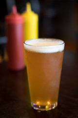 Pint of beer with ketchup and mustard bottles in the background
