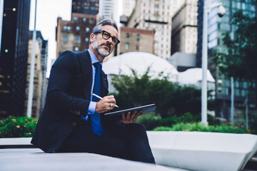 Adult businessman holding tablet and stylus on street