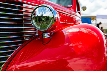 Old vintage American bright red pickup car front side close up view, with chrome glass headlights...