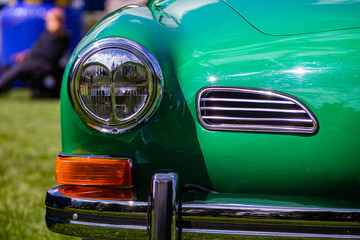 Fototapeta na wymiar Bright green old classic antique American car half front, left side, close up on glass headlights and signals lights lamps and chrome bumper