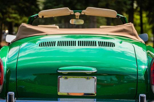 classic antique American green Convertible car rear selective focus with open roof against blurred trees background, during outdoor old cars show