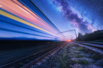 High speed train in motion and Milky Way at starry night. Industrial landscape with sky and stars...