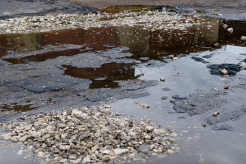 Asphalt road in city with a huge pit and puddle