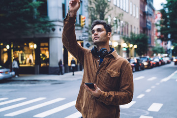 Ethnic young man catching taxi on crossroad