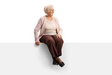 Elderly woman sitting on a blank panel and looking to the side