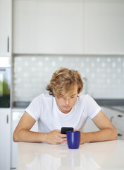 Teenage boy typing text message.Sitting in the kitchen.Using smart phone
