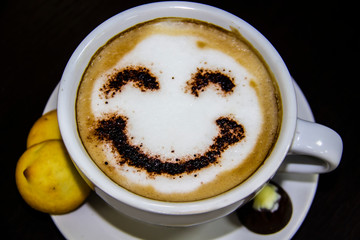 the cup of coffee with smile on the table. The biscuits with candy. Smile. Be happy with coffe