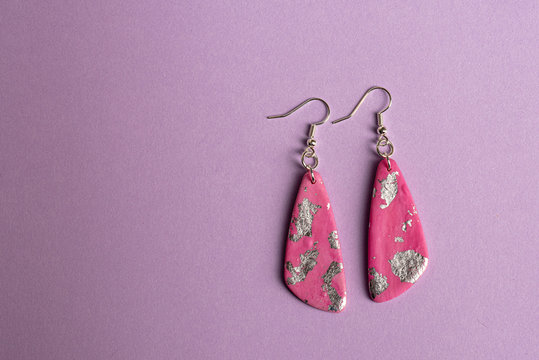 Pink and silver earrings on purple background.