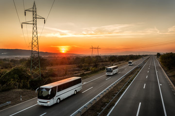 Caravan or convoy of Four buses in line traveling on a country highway under amazing orange  ...