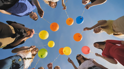 A group of friends release colorful balloons into the sky.