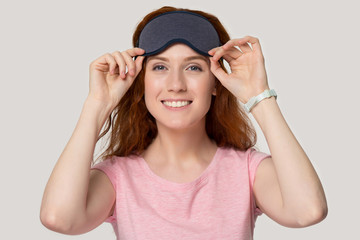 Happy millennial red-haired woman holding sleeping eye mask on forehead.