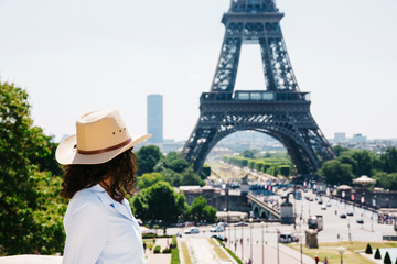 Caucasian female model with blue dress and cowboy hat in front Eiffel tower at Square du Trocadéro. Blue and cloudy background at mid-day