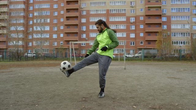 Slow motion shot of middle eastern athlete with ponytail masterly juggling soccer ball on outdoor sports field on autumn day