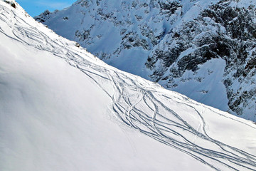 snowboard tracks on a snowy mountainside on sunny day