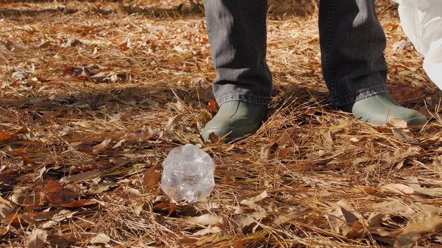 Volunteer worker picking up litter in the woods with trash picker tool. Outdoor garbage collection from forest park. Plastic bottle and plastic bag pollution removal and ecological clean up.