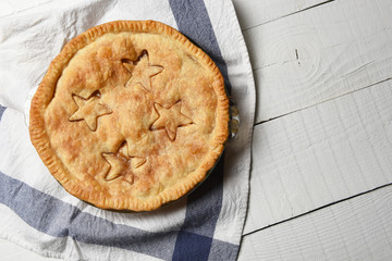 High angle shot of a fresh baked homemade apple pie on a white wood table and tea towel.
