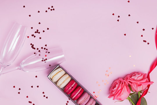 Two Champagne Glasses, Macarons, Roses And Heart Shaped Confetti On Pink Background.