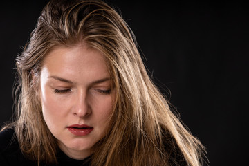 young beautiful blonde girl with a calm expression and closed eyes on a dark background, copy space