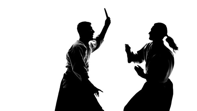 Black silhuettes of two males in keikogi or kimono showing aikido using tanto. Isolated, white. Slow motion. Close up.