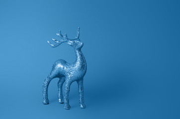 Sparkling deer decoration for Christmas. Deer figurine isolated on blue background. Christmas symbol. Decorations deer. Silver glitter stag decoration. Color of the year 2020 classic blue.