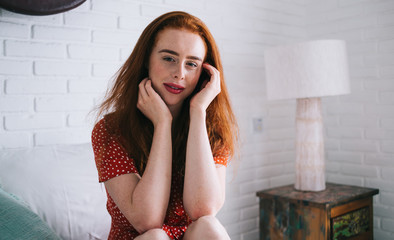 Happy and glad red haired woman sitting on bed