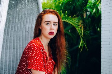 Thoughtful red haired woman sitting in wicker chair