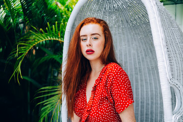 Alluring woman in red dress sitting on swing chair in garden