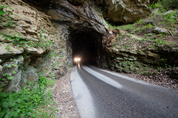 Dangerous Driving. Headlights of car exiting one lane tunnel on a narrow wet mountain road in...