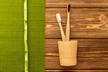 Fototapeta na wymiar Bamboo toothbrushes in hand made clay glass bamboo plant with green towel on wooden background.Flat lay copy space. Biodegradable natural bamboo toothbrush. Eco friendly, Zero waste, Dental care