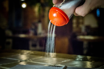 Salt is poured down from the salt shaker. In the cafe