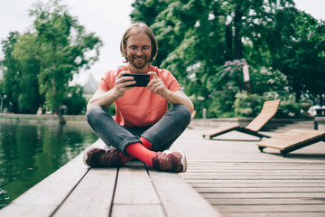 Cheerful man watching video on smartphone on pier