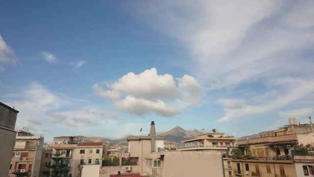 Smooth timelapse video of white clouds over Sicilian houses with mountains in the background.