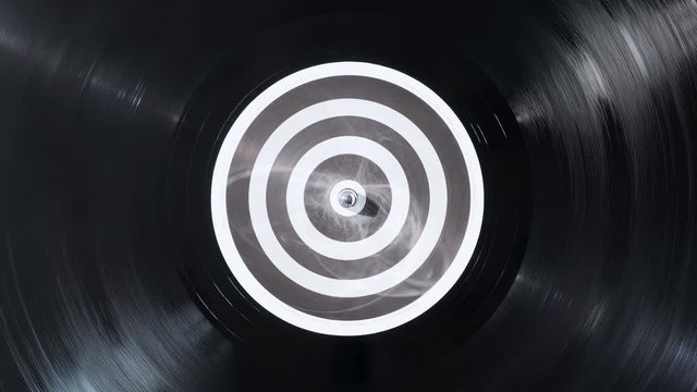The vinyl record on DJ turntable record player close up. Black vinyl background with a black and white screen in center. The rotating plate and stylus with the needle close-up. Loop. Macro. View above
