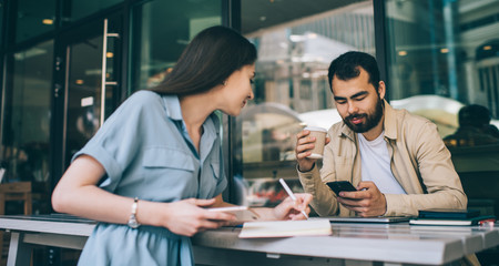 Female freelancer making notes near colleague with smartphone