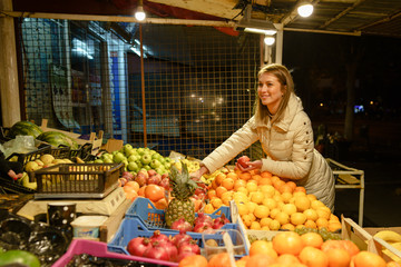 One young caucasian woman female girl picking some fresh fruit at the local market in the city at in autumn spring or winter night