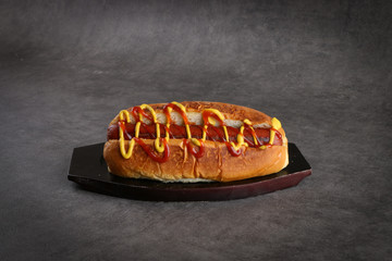 Sausage sandwich with mustard and ketchup on a dark gray background