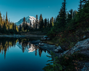 Volcano Mt Rainier reflecting in pristine alpine lake with the moon