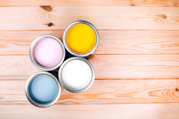Four open cans of paint on wooden natural background. Yellow, white, pink, turquoise colors. Top view.