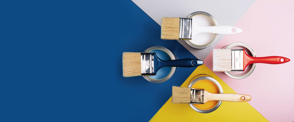 Banner with four open cans of paint with brushes on them on bright symmetry background. Yellow, white, pink, blue colors of paint. Top view. - obrazy, fototapety, plakaty