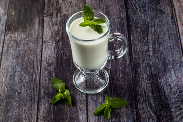 Ayran in a glass, sour-milk drink, yogurt, decorated with a leaf of mint. On a wooden background