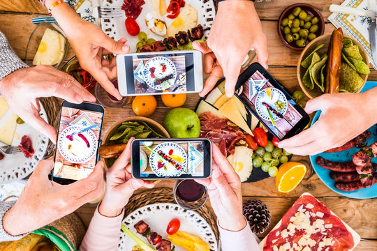 Group of unrecognizble friends or family caucasian people having fun together taking picure at their dishes with food - home or restaurant concept of people having fun with technology and media